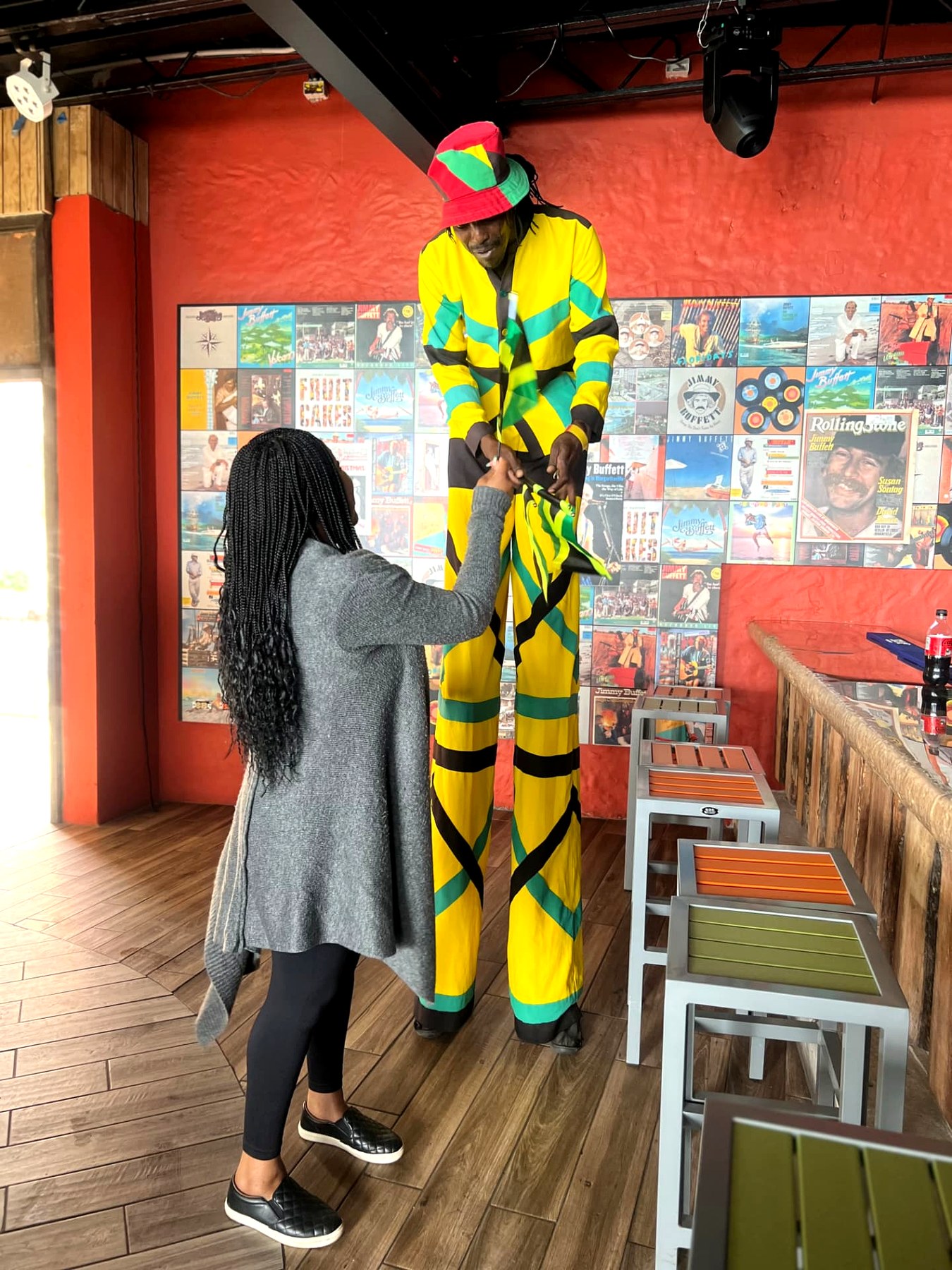 Me greeting a stilt walker in a yellow, green and black Jamaican outfit inside a bar in Montego Bay