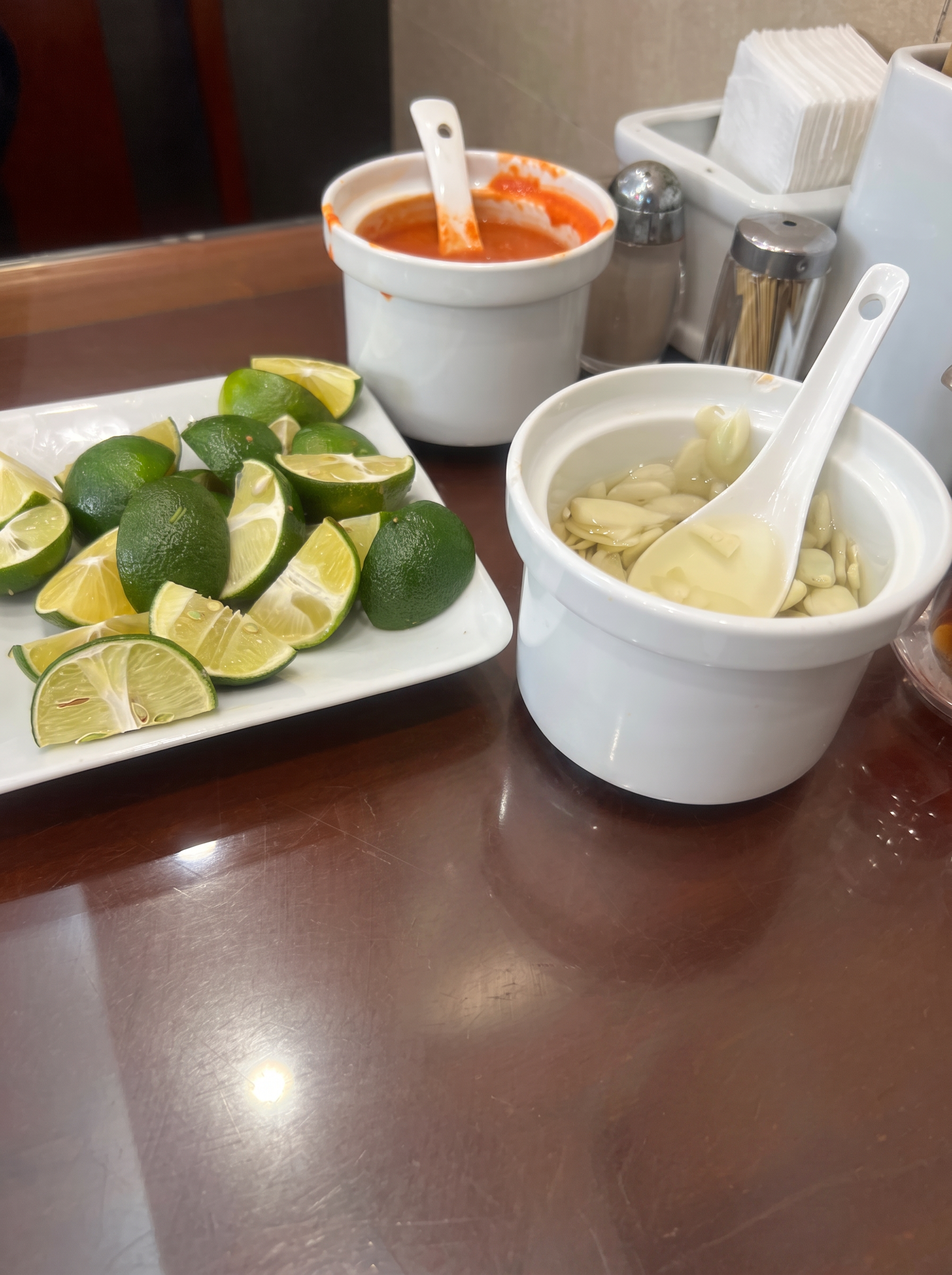 Plate of lime wedges, chili sauce and pickled garlic on the table at Pho 10 in Hanoi
