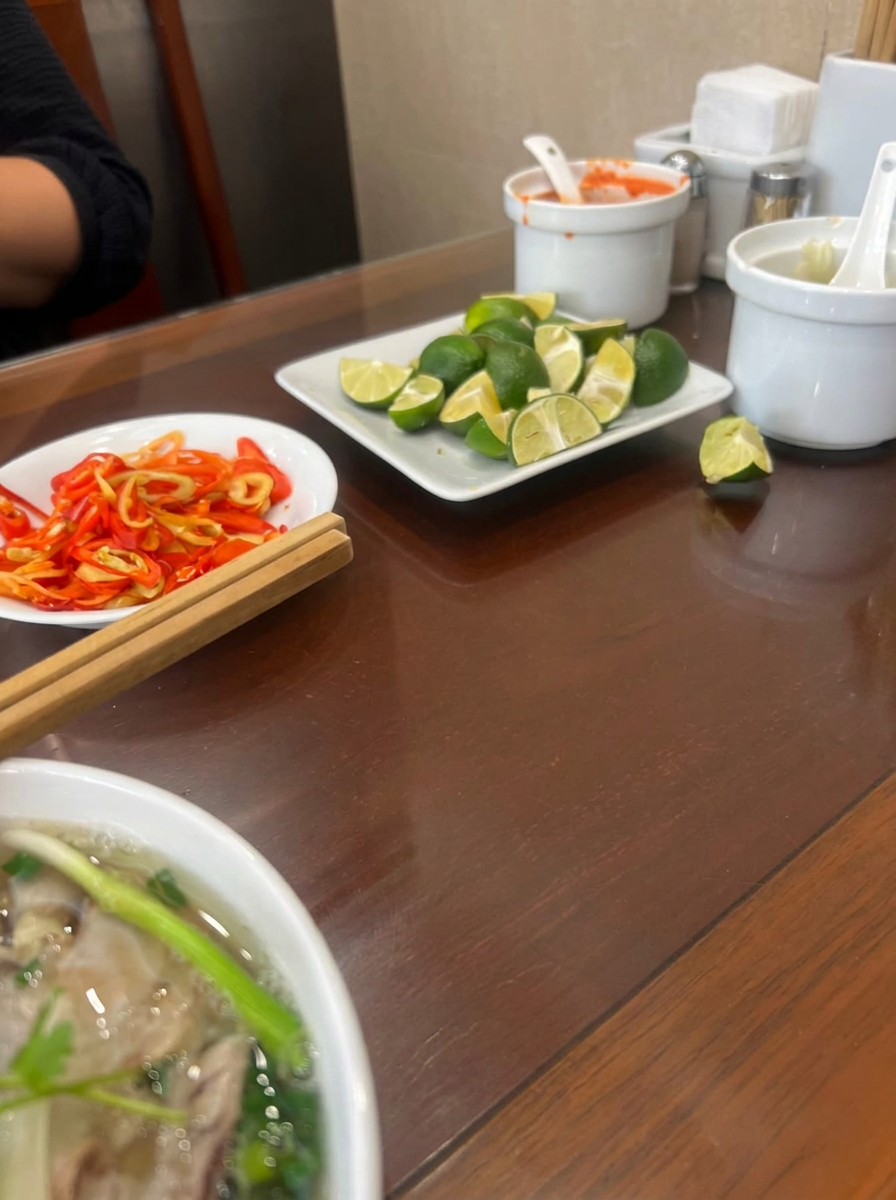 Limes and sliced chilies on the table next to a bowl of pho
