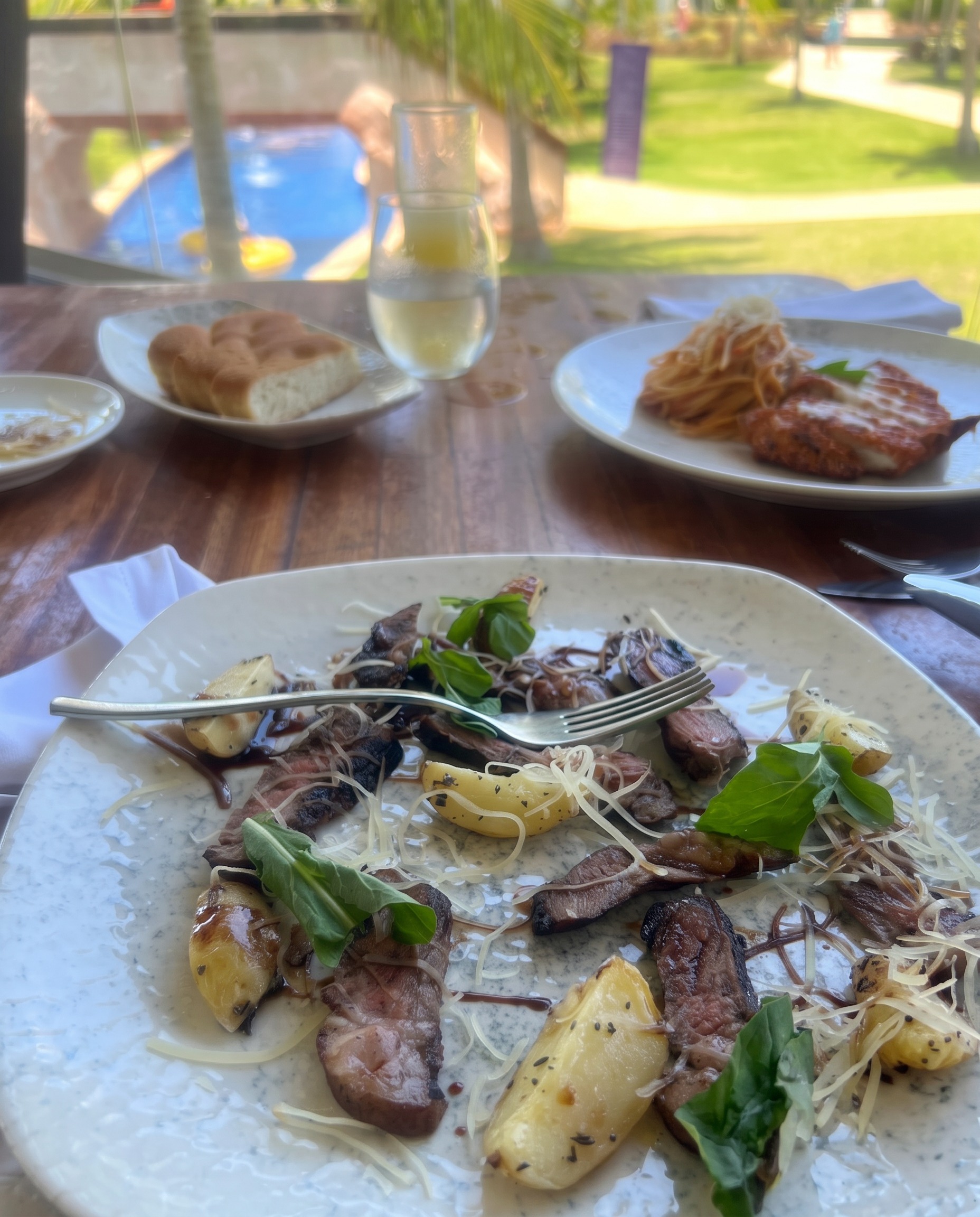 A plated steak and potato dish on the resort restaurant table with the pool and gardens outside