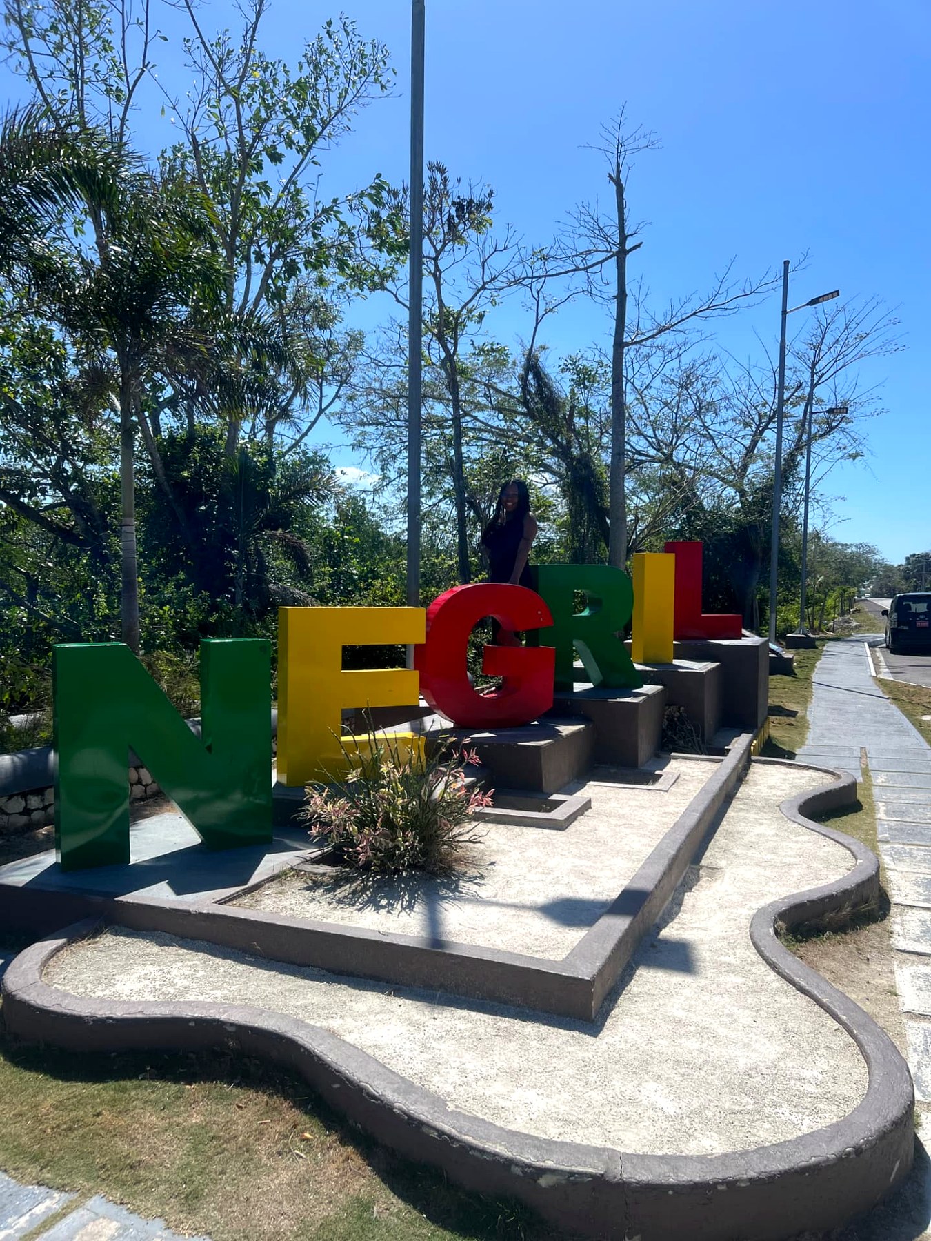 Me standing behind the colourful green, yellow and red NEGRIL letter sign on the roadside