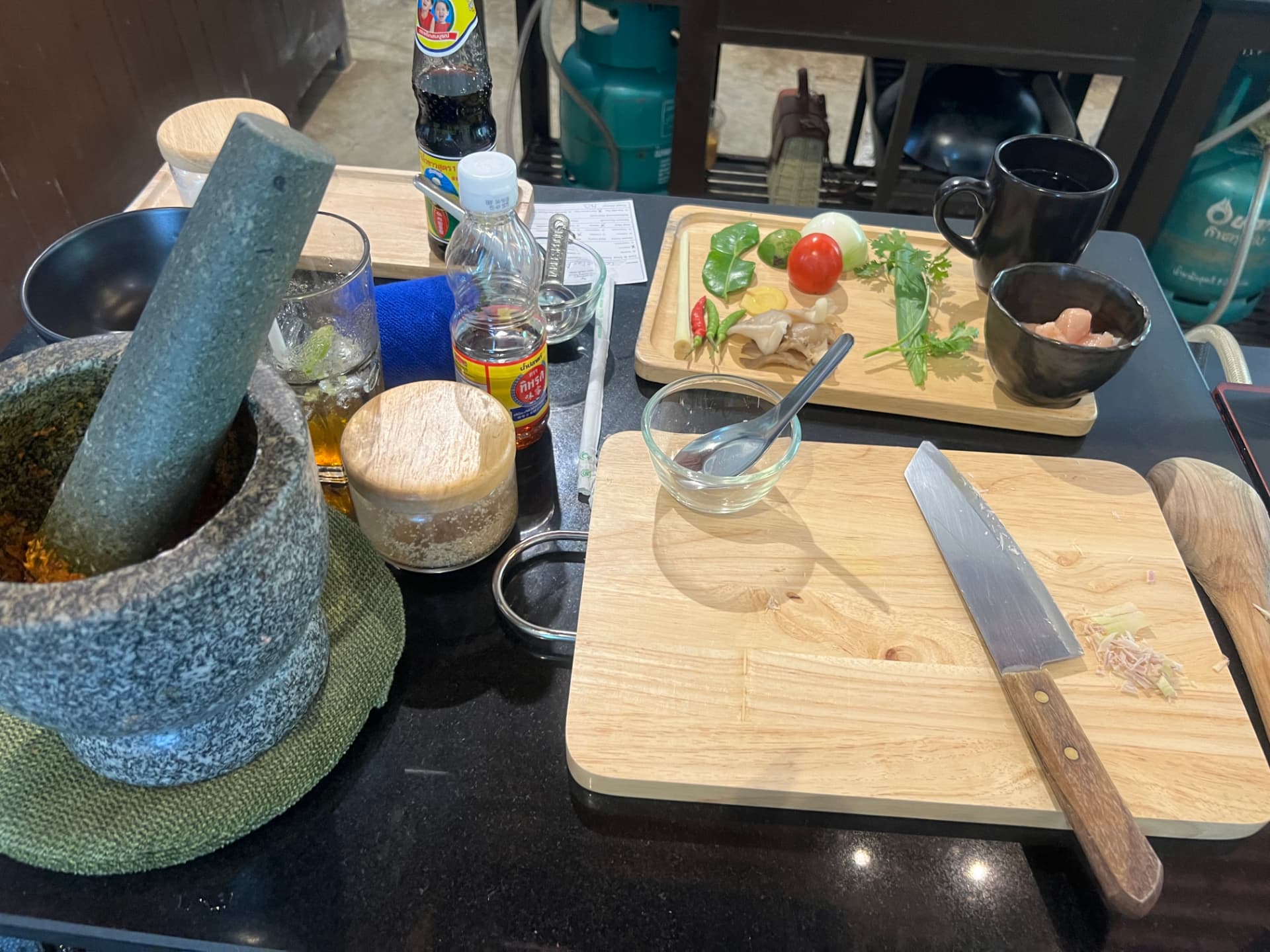 Tray of fresh Thai ingredients — kaffir lime leaves, lemongrass, chilies, tomato, cilantro and chicken — beside a mortar of curry paste
