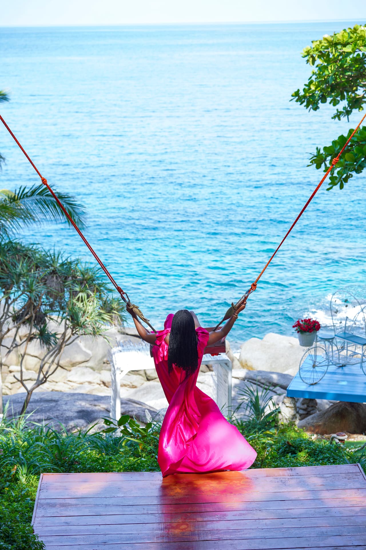Jenn on a swing in a pink floating dress above the ocean in Phuket