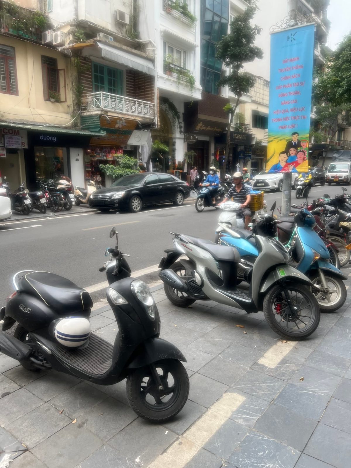 Mopeds parked along the sidewalk and riding through traffic in Hanoi