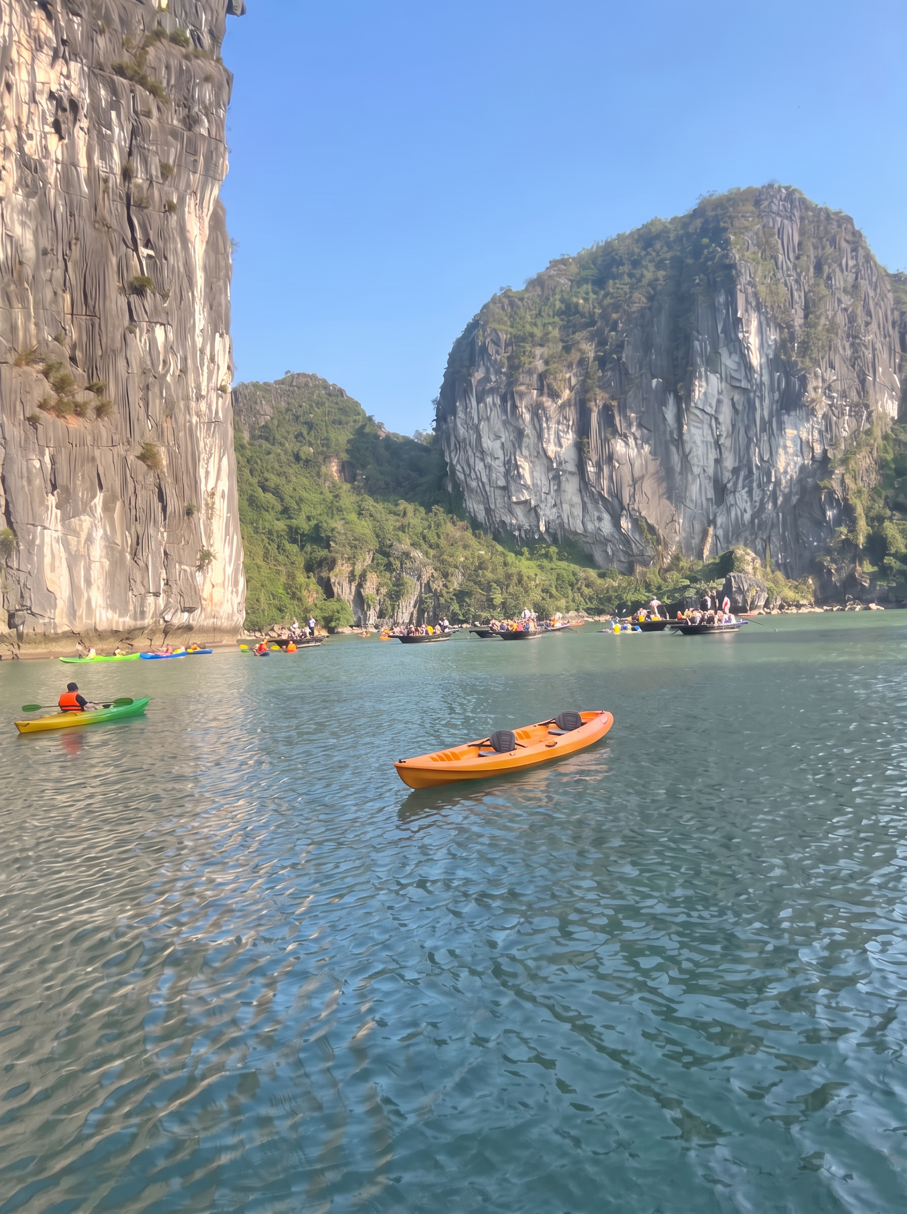 Kayakers and small rowed boats between limestone cliffs in Ha Long Bay